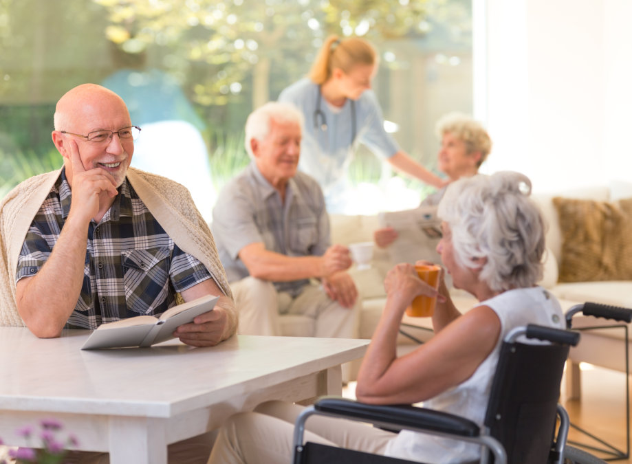 Elder men with a book talking to disabled women drinking tea