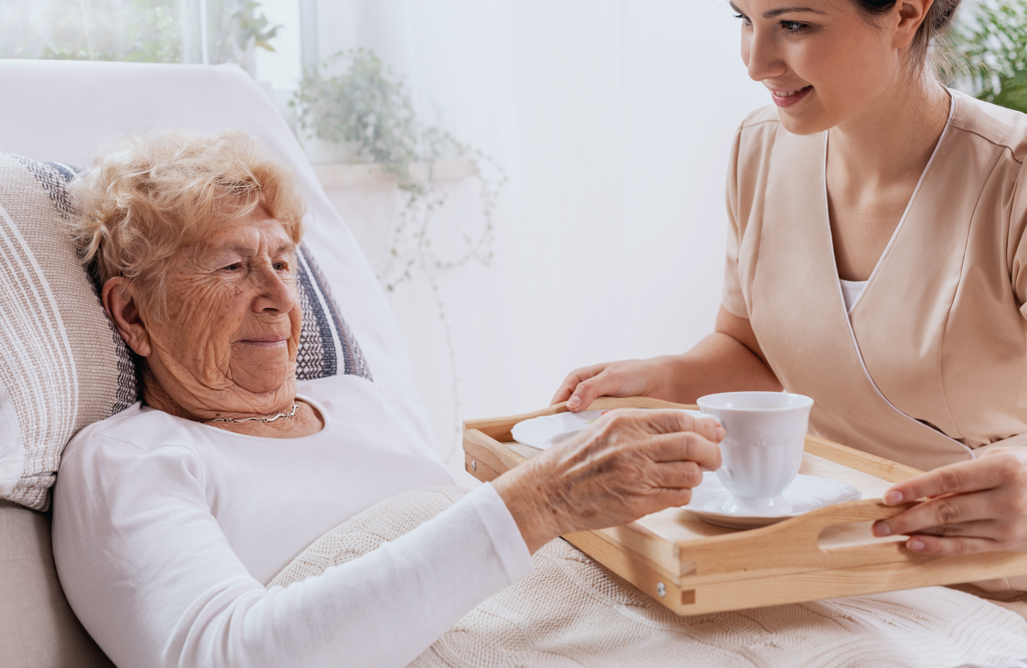nurse giving coffee to elderly woman in bed - Maple Care Homes residential assisted living